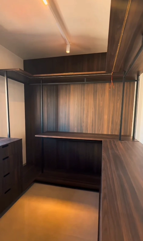 Registro da marcenaria do closet em execução, com painel amadeirado, cabideiros e superfícies de apoio.