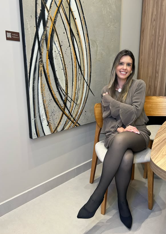 Cauanne Brandi sentada junto a uma obra de arte e mobiliário em madeira.